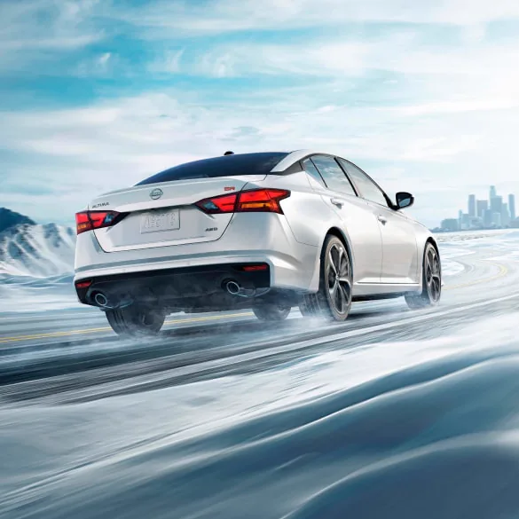 2027 Nissan Altima in white seen from behind driving in snowy landscape illustrating all-wheel drive at Faulkner Nissan of Harrisburg in Harrisburg PA